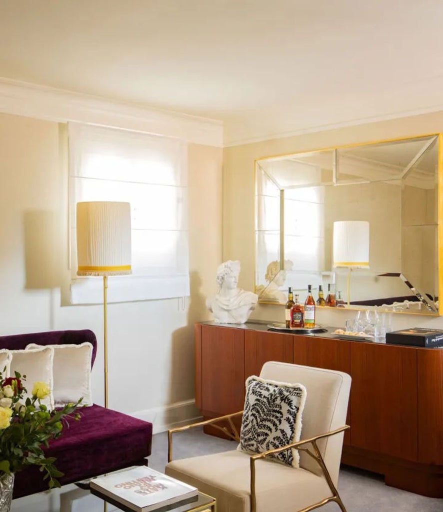 Elegant hotel suite with ornate gold-framed mirrors, emerald velvet headboard, crystal chandelier and marble side tables in warm lighting