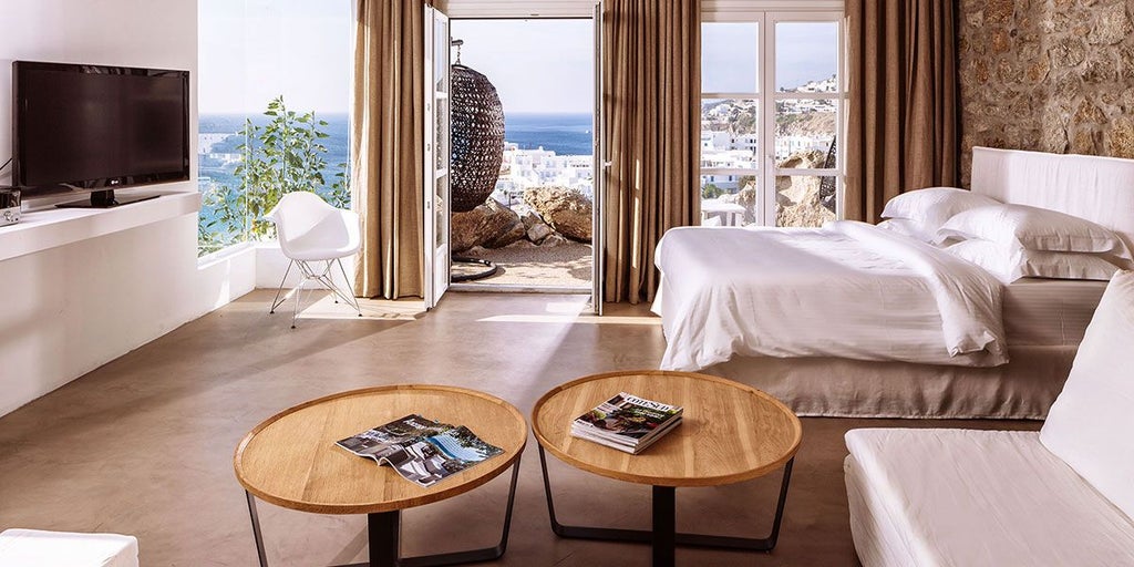 Luxurious blue-toned Azure Suite with panoramic Aegean Sea view, sleek modern design, minimalist white furnishings, and floor-to-ceiling windows at Scenset Hotel, Greece