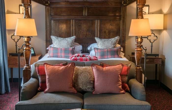 Elegant cottage-style hotel room with plush white bedding, soft neutral tones, antique wooden furniture, and classic British countryside charm at a luxury boutique hotel