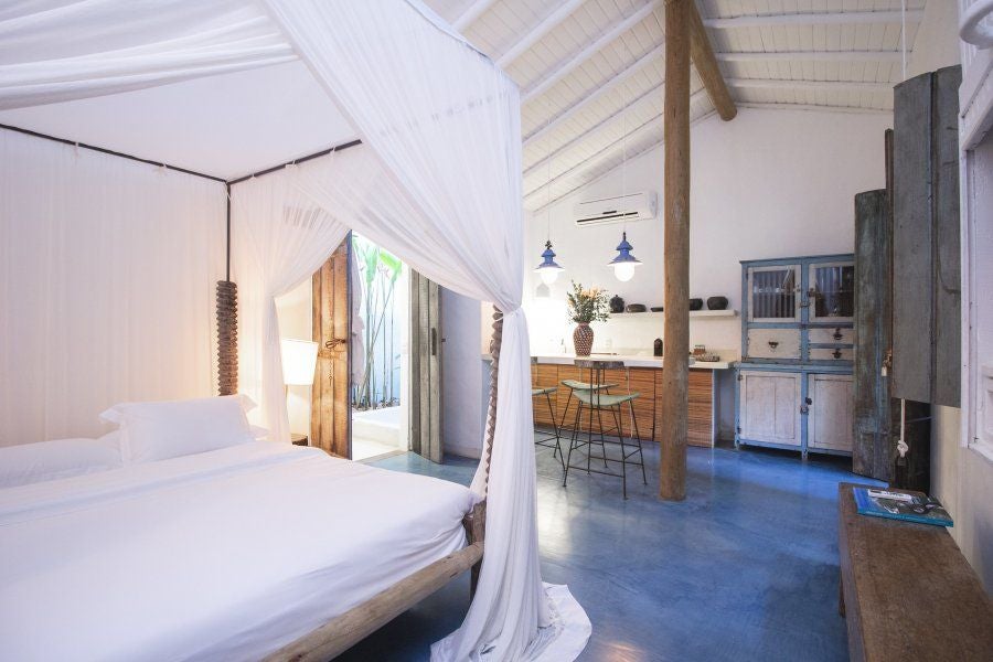 Rustic wooden bed with white linens in a sunlit Brazilian luxury hotel room at UXUA Casa Hotel, featuring traditional Trancoso-style decor and natural textures