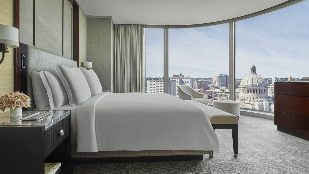 Spacious accessible hotel suite with elegant Four Seasons decor, featuring floor-to-ceiling windows overlooking Boston's Back Bay skyline, modern amenities, and sophisticated design