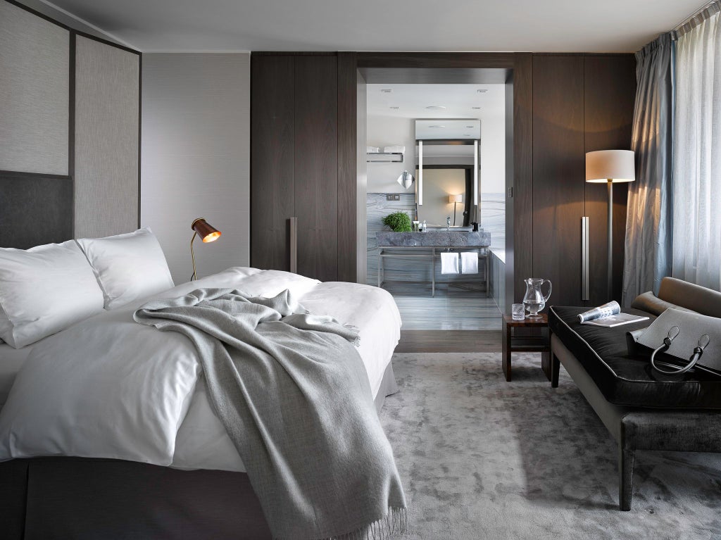 Elegant petite hotel room with soft gray walls, plush white bedding, modern minimalist design, and city view window in The Emblem Prague luxury hotel