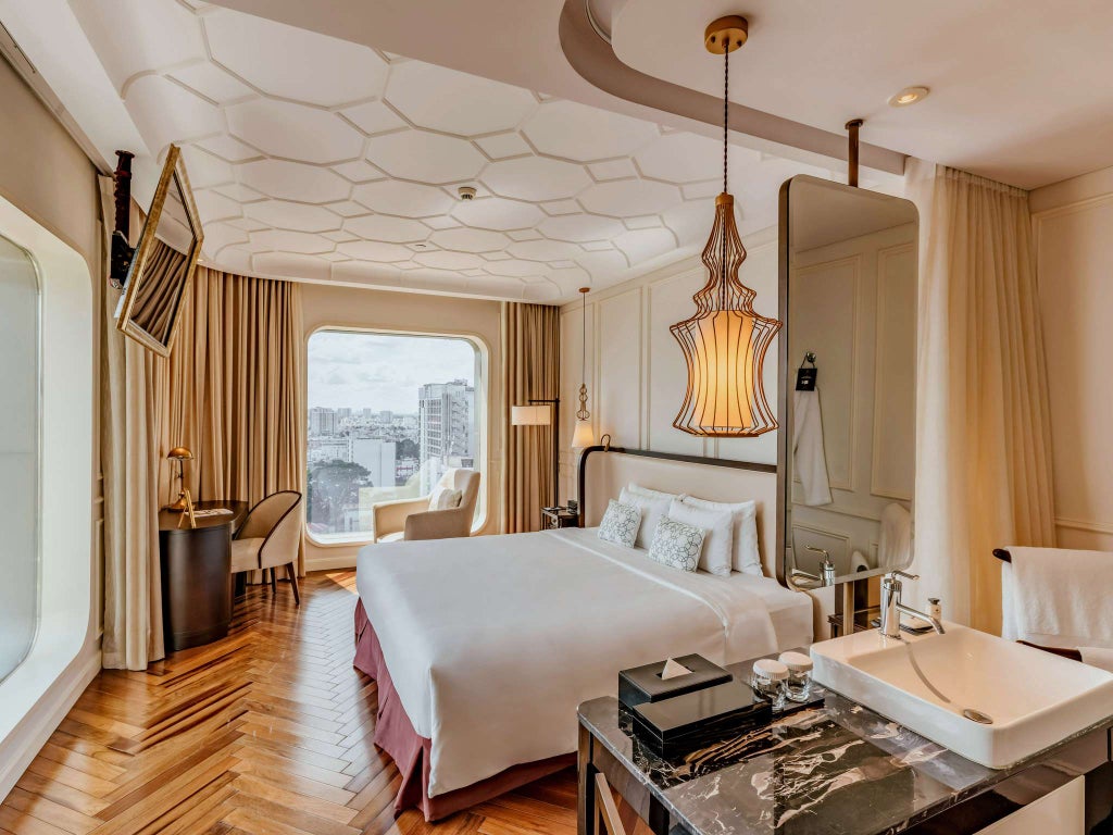 Luxurious corner hotel room with floor-to-ceiling windows, king bed, modern Vietnamese decor, and panoramic Saigon city skyline views