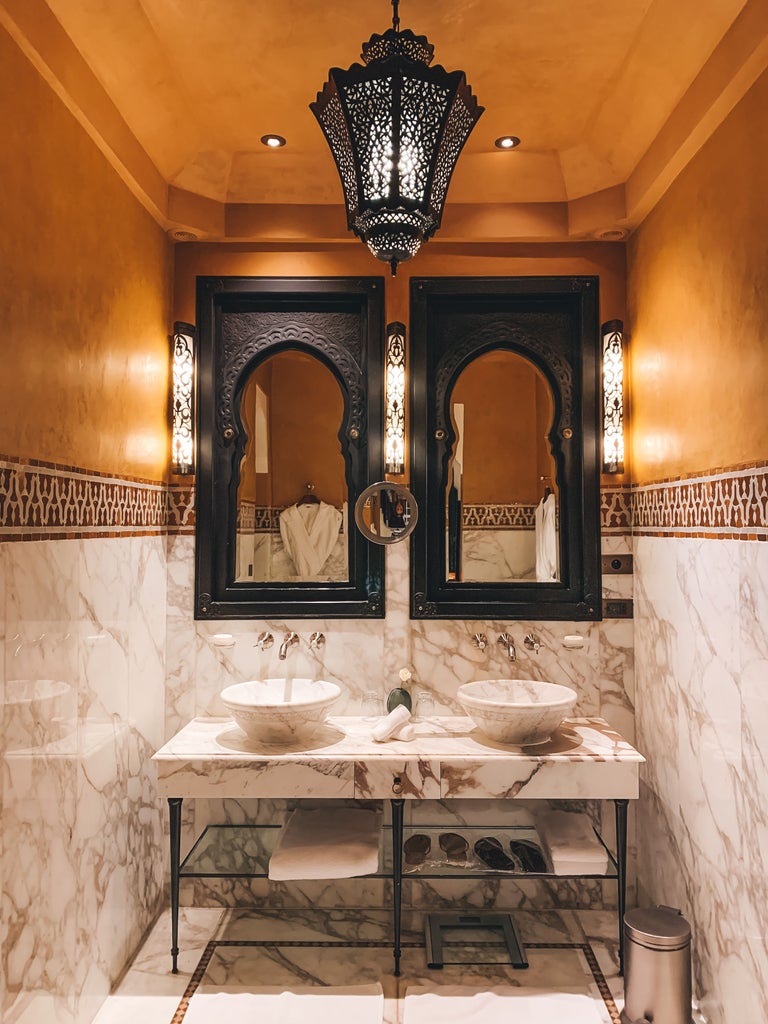 Ornate Moroccan archways frame a tranquil courtyard garden with symmetrical palm trees and fountains at luxury hotel La Mamounia