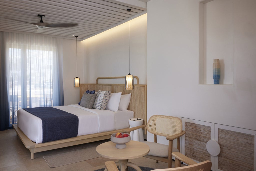 Elegant hotel suite with floor-to-ceiling windows, modern furnishings, white linens, and panoramic views of the Mediterranean Sea.