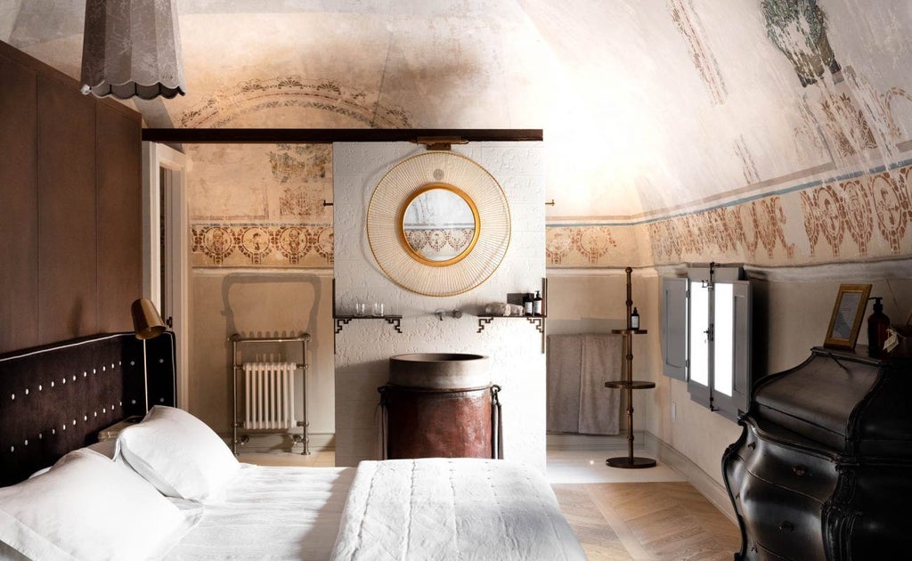 Elegant Italian boutique hotel suite with plush white bed, marble bathroom, ornate architectural details, and soft natural lighting from large windows.