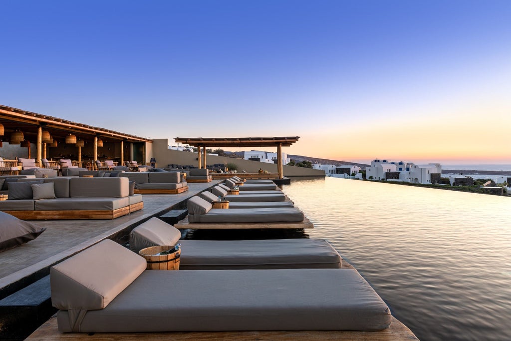 An infinity pool overlooking the Aegean Sea at sunset, with white Santorini architecture and lavish loungers on the terrace