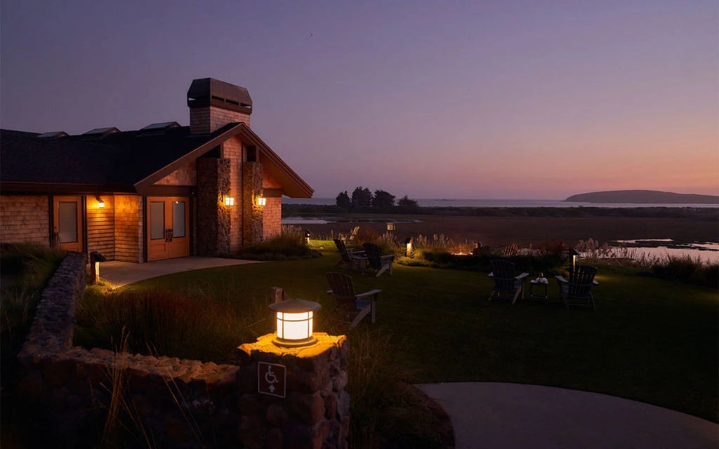 Luxurious coastal lodge nestled in Bodega Bay, featuring rustic wooden exterior, panoramic ocean views, and elegant landscape with lush greenery at sunset