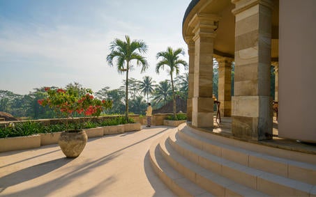 Elegant stone pavilions with traditional Javanese architecture overlook misty volcanic mountains at sunrise, central dome echoes Borobudur temple