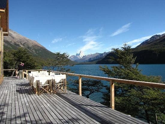 Rustic-luxe lodge with wooden facade nestled at base of snow-capped Andes mountains, reflecting in pristine Patagonian lake waters