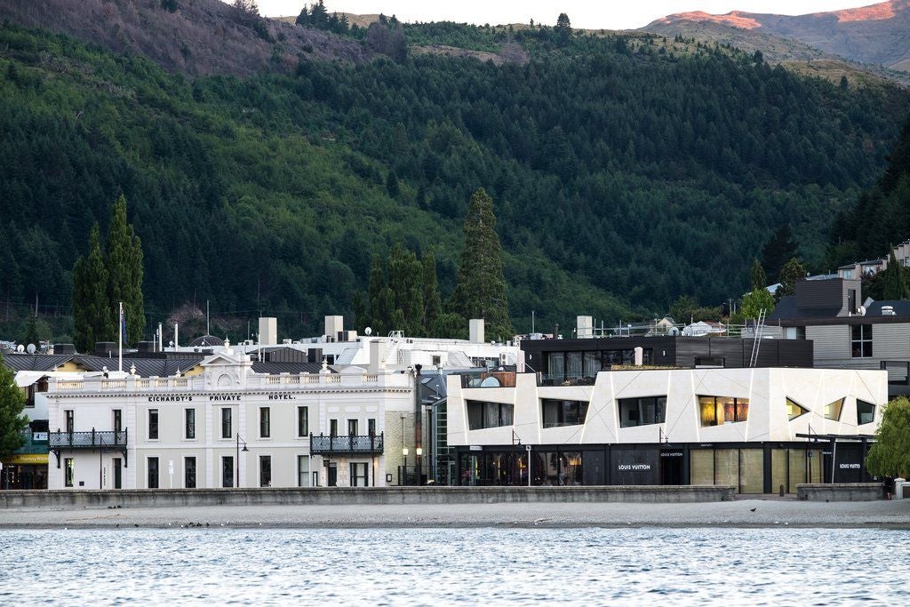 Elegant Victorian-era lakeside hotel with white stone facade, ornate windows and balconies overlooking Lake Wakatipu in Queenstown