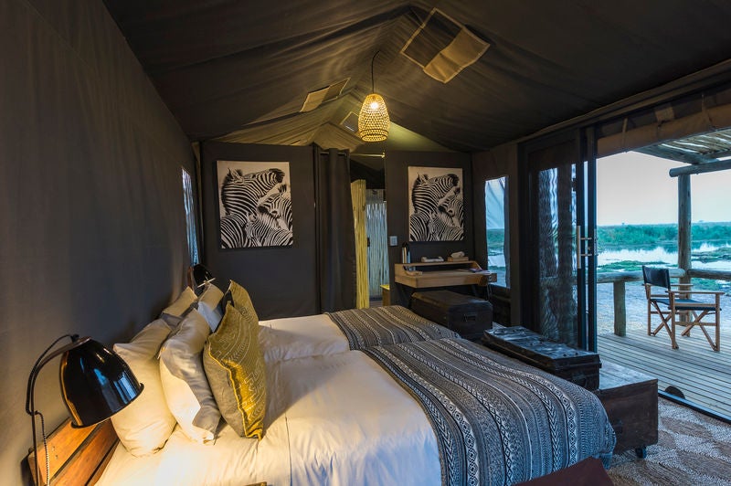 Luxurious safari tent overlooking Linyanti marshlands at sunset, with wooden deck, canvas walls and elegant outdoor furniture