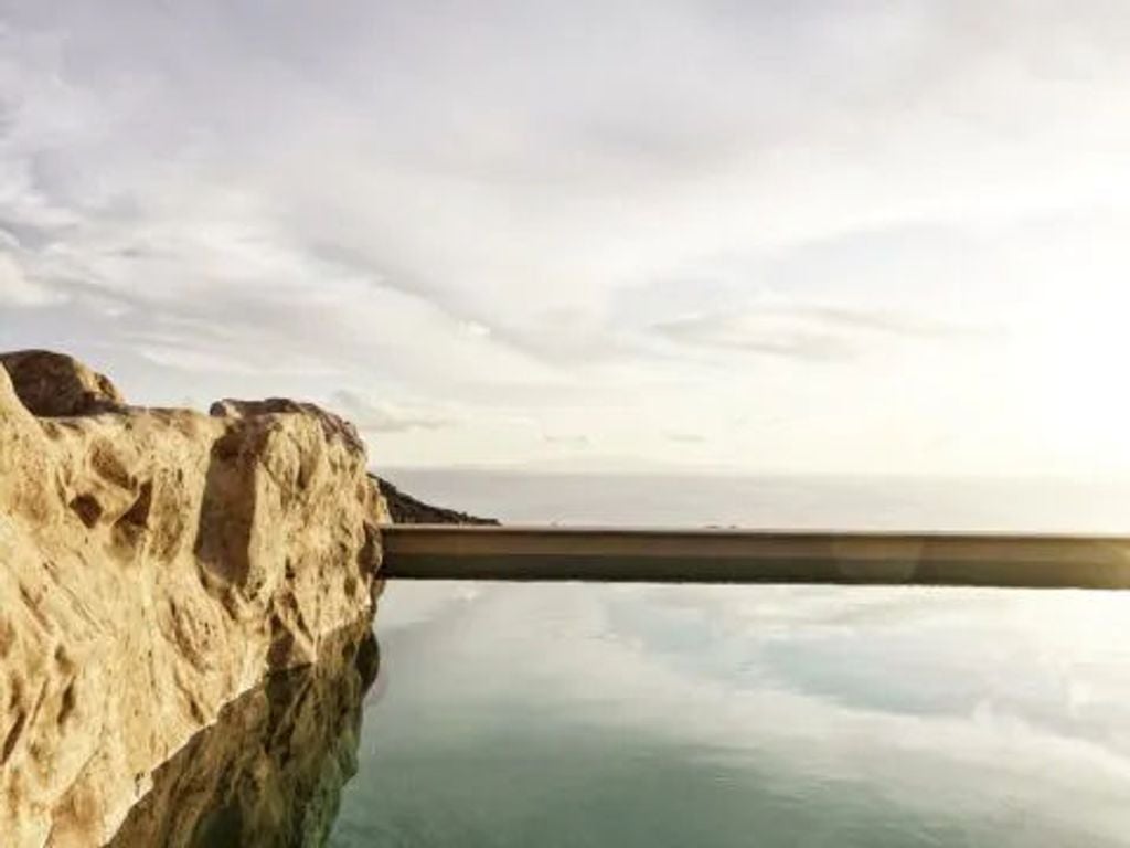 Modern whitewashed hotel suite with curved walls, private infinity pool overlooking the Aegean Sea and Santorini caldera at sunset