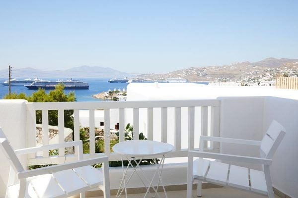 Luxurious whitewashed Cycladic hotel overlooking azure Mykonos waters, with elegant curves, blue-domed architecture, and pristine infinity pool at sunset