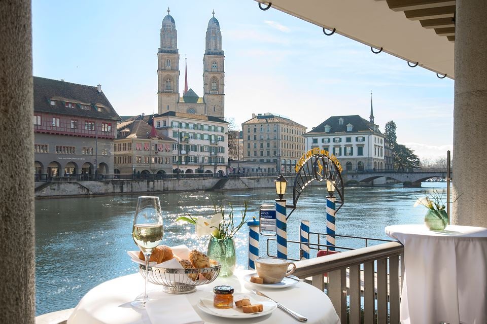 Historic Storchen Hotel with elegant white facade and traditional Swiss architecture overlooks Limmat River in Zurich's old town at sunset