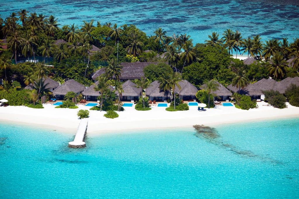 Luxurious overwater villas with private decks connected by wooden walkways over crystal-clear turquoise Maldivian lagoon at sunset