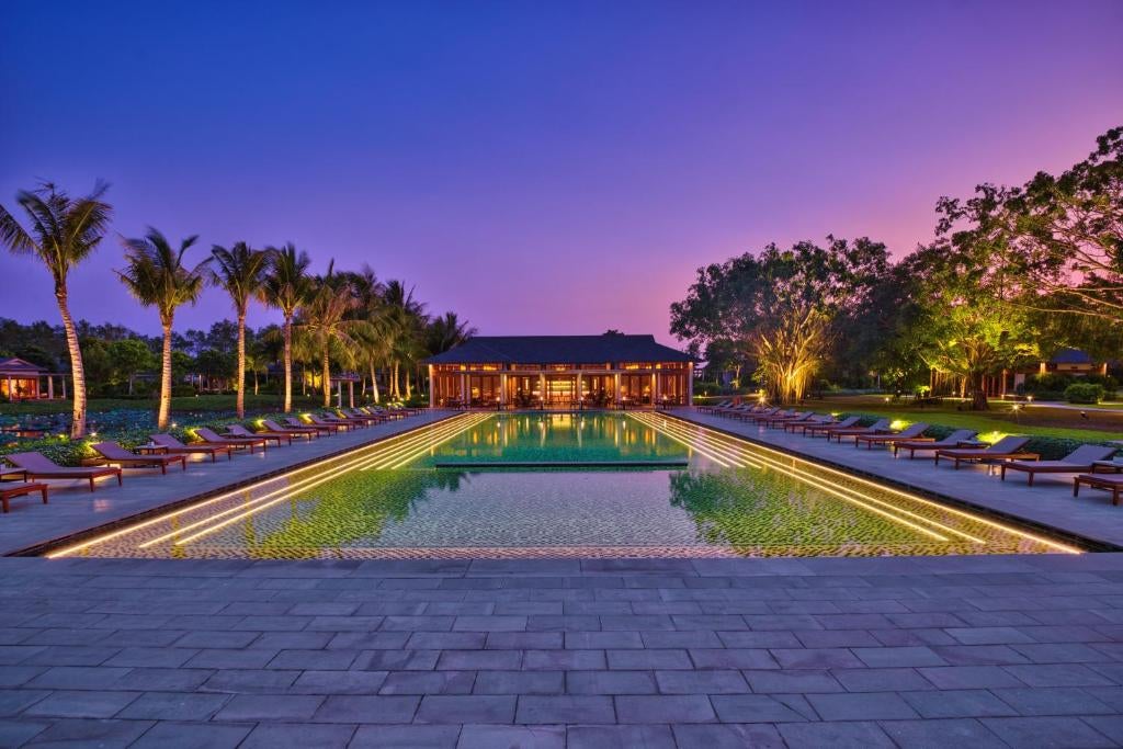 Elevated overwater villas with thatched roofs surrounded by palm trees at luxury Mekong Delta resort, reflecting in calm waters