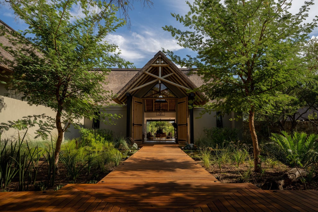 Five-star safari lodge with thatched roof and wooden deck overlooking a tranquil waterhole in the South African bushveld at sunset