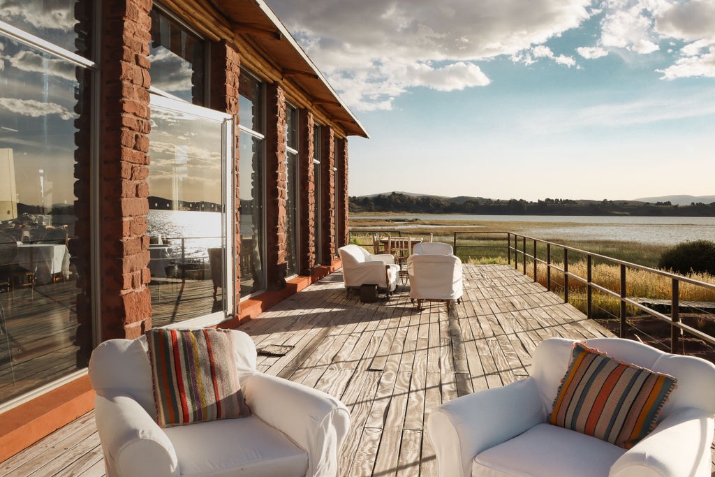 Modern luxury lodge with stone walls and floor-to-ceiling windows overlooking Lake Titicaca, featuring private terrace and local decor