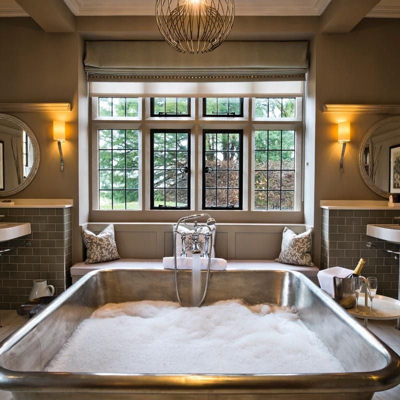 Elegant oak-paneled bedroom at luxury manor, featuring plush bedding, antique furniture, and expansive countryside views through large windows