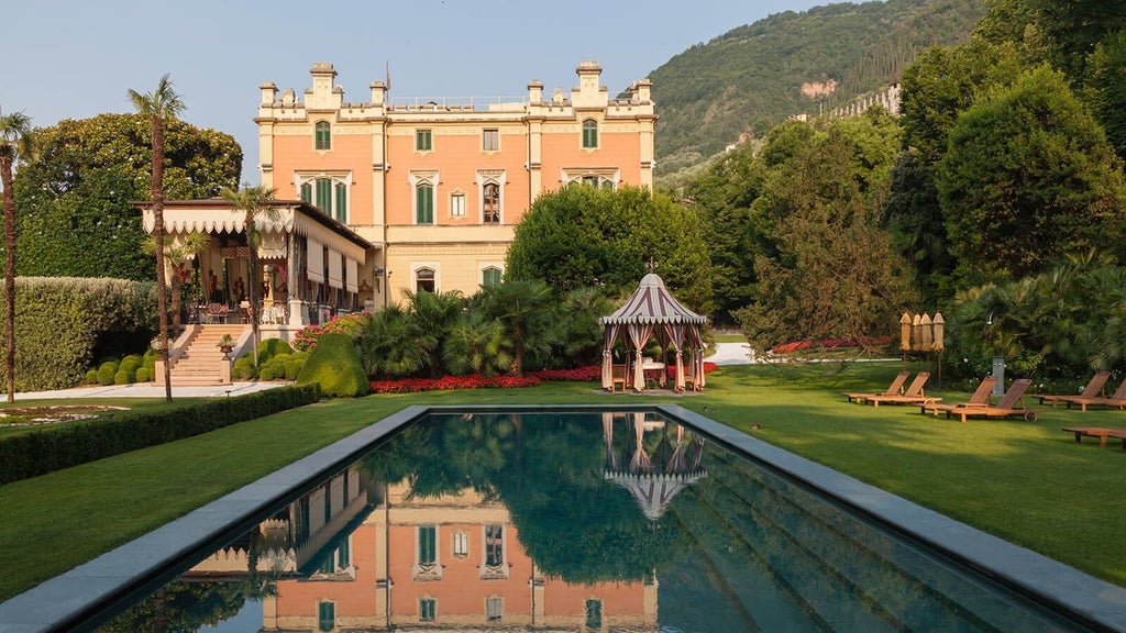 Modern Italian hotel with terracotta roof and elegant stone facade nestled in lush hillside gardens overlooking Lake Como at sunset