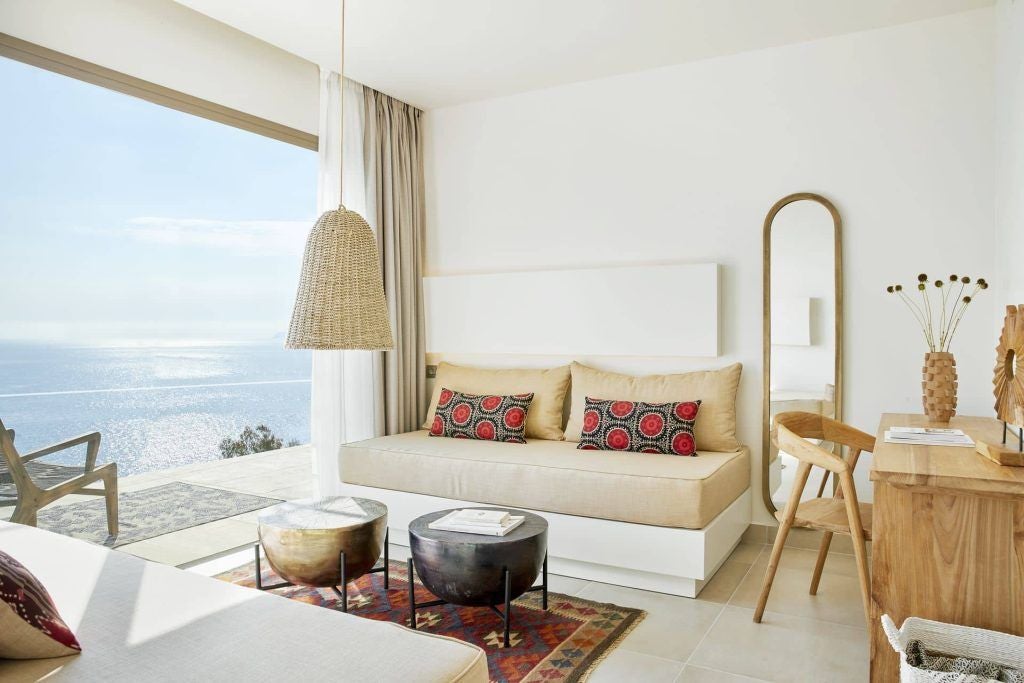 Modern luxurious one-bedroom suite with elegant white decor, featuring a spacious bedroom, minimalist design, and panoramic sea view in Greece.