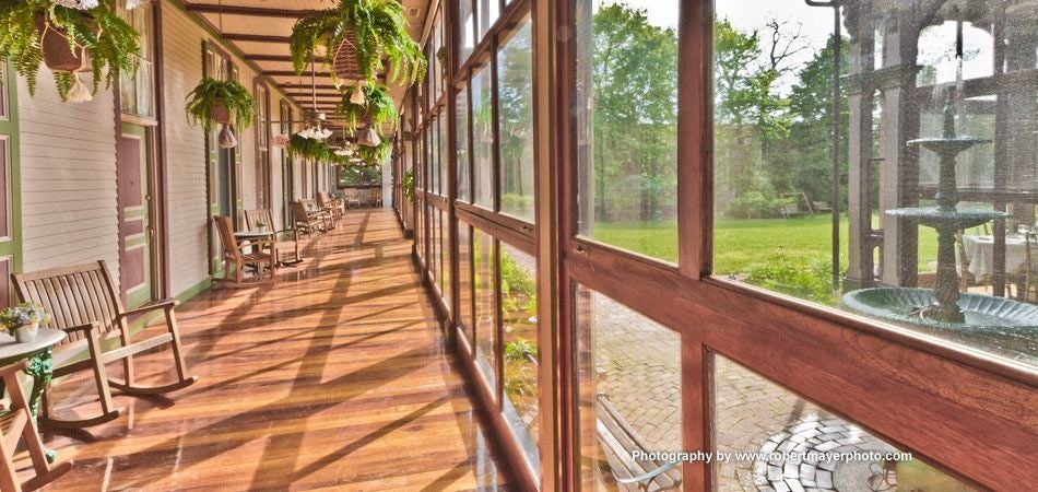 Elegant antebellum mansion with white columns, wraparound veranda, manicured gardens, and ornate iron fencing set in lush Southern landscape