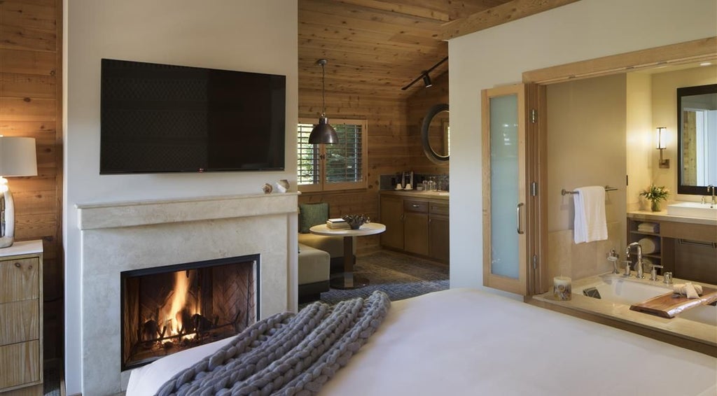 Luxurious fireplace-equipped guestroom with natural wood accents, plush bedding, and panoramic views of coastal forest at Ventana Big Sur, California