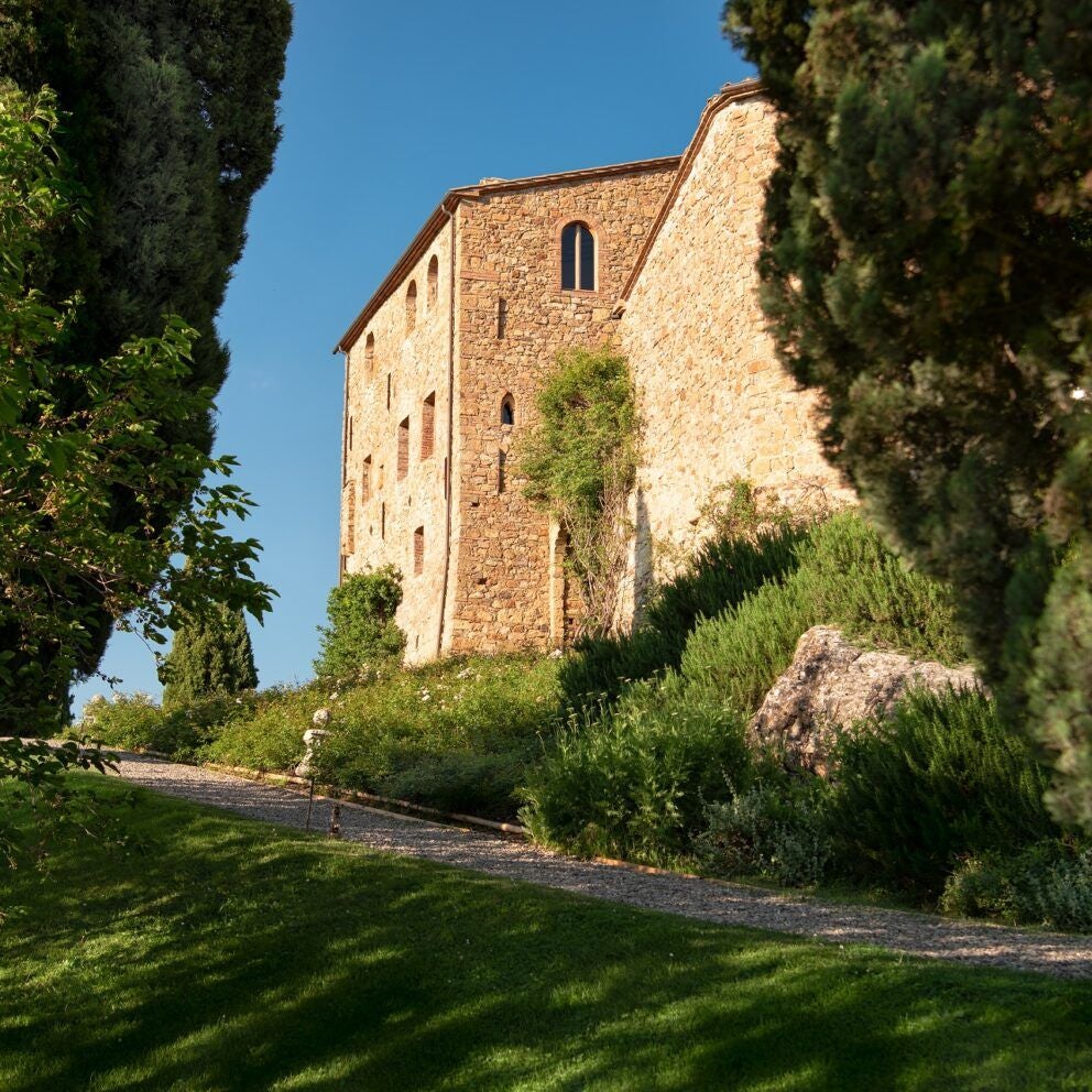 Rustic stone Tuscan castle with terracotta roof, surrounded by rolling vineyards and cypress trees at golden sunset