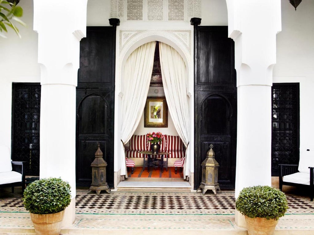 Elegant Moroccan riad with white archways framing lush courtyard garden, antique lanterns, and central fountain under an open-air atrium