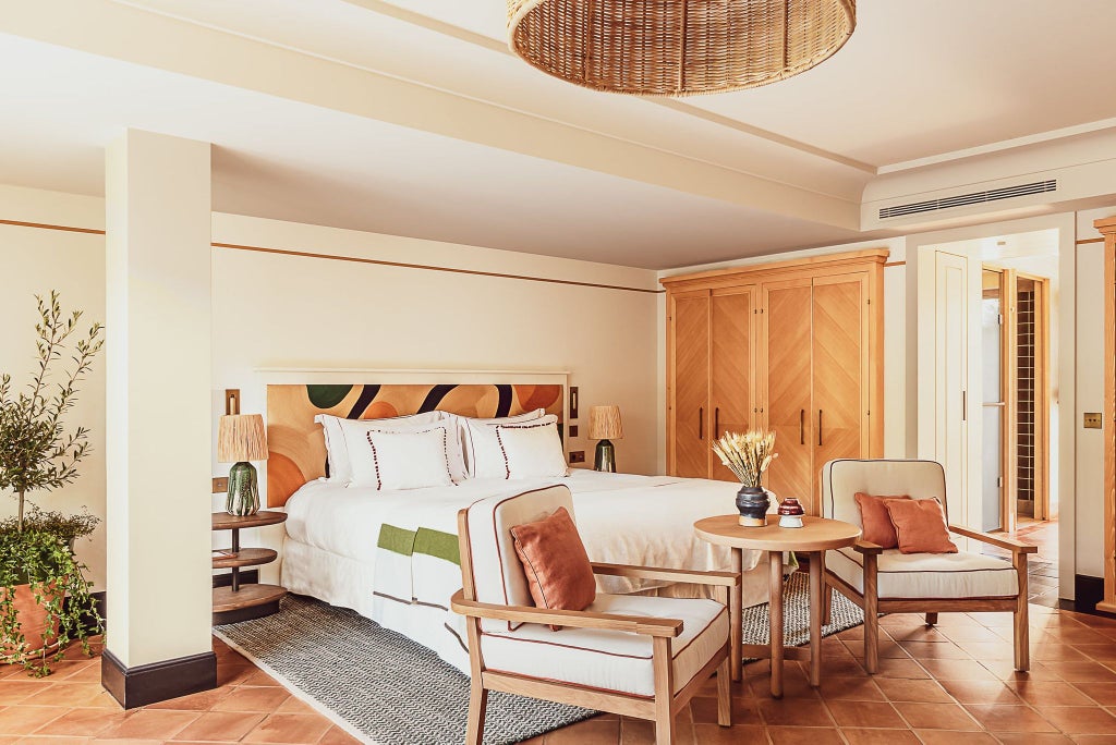 Elegant prestige junior suite at Lou Pinet, featuring plush white bedding, warm wood tones, and subtle French Riviera-inspired design elements