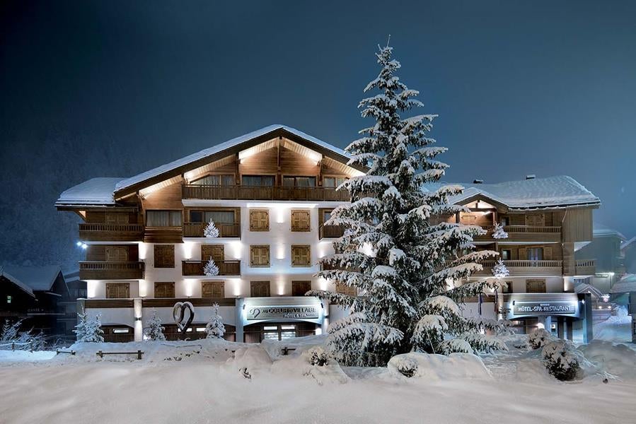 Elegant alpine spa hotel with wooden balconies and stone facade nestled in French village, snow-capped mountains in background