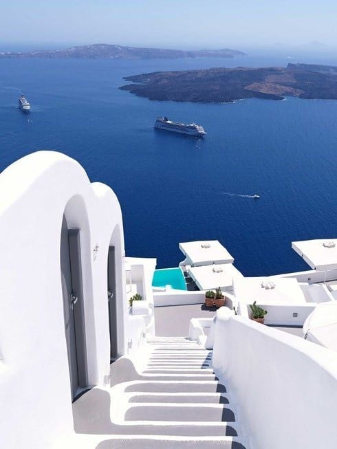 Whitewashed luxury suites with infinity pools cascading down Santorini's volcanic cliffs, overlooking the azure Aegean Sea at sunset