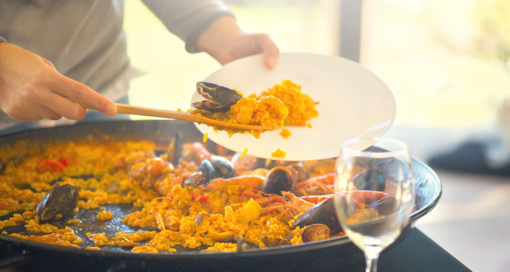 A chef and student in crisp white aprons craft Spanish tapas at a high-end kitchen counter with polished copper cookware overhead