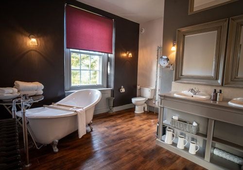 Elegant boutique hotel room with wooden floors, crisp white bedding, and large windows overlooking countryside in a luxury Yorkshire Dales setting