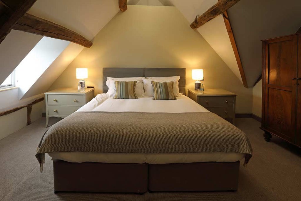 Elegant suite at Kings Head Hotel with plush king bed, rich hardwood floors, tasteful decor, and expansive window overlooking scenic UK countryside landscape