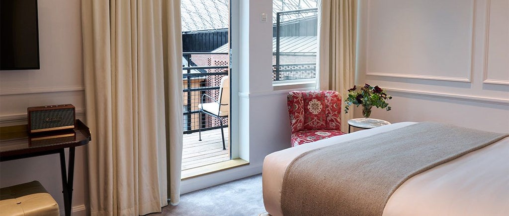 Elegant Swedish hotel room with plush king bed, soft neutral tones, stylish wooden furniture, and a private balcony overlooking tranquil urban landscape