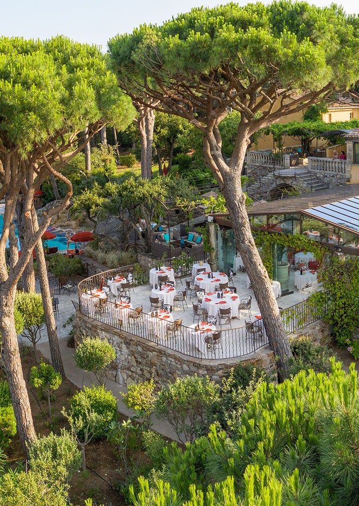 Luxurious seaside villa with white facade, lush tropical gardens, and blue-tiled pool overlooking the Saint-Tropez coastline at golden hour