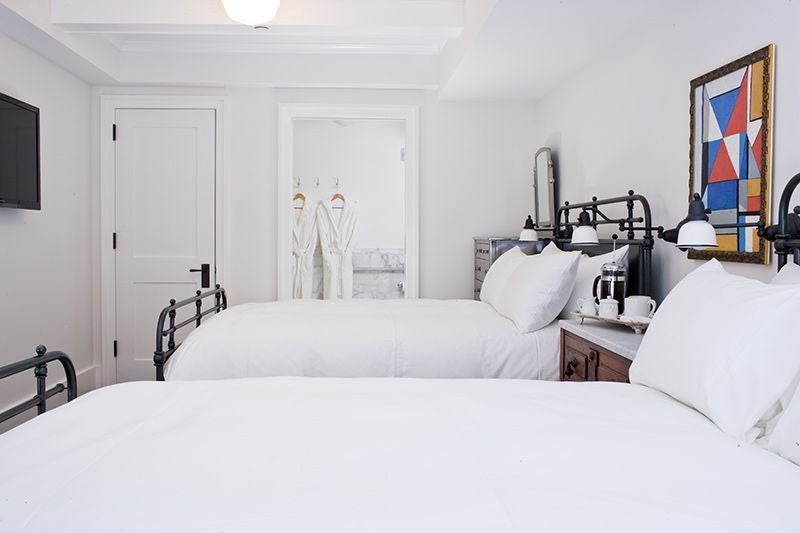 Elegant two-queen hotel room with modern decor, soft neutral colors, plush bedding, large windows, and sophisticated minimalist design in a luxury boutique setting.