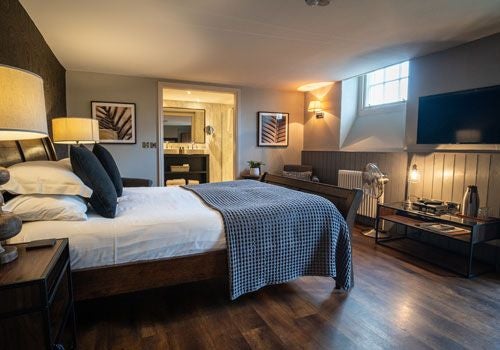 Elegant bedroom at scenset House in rural United Kingdom, featuring plush white bedding, wood-paneled walls, and soft natural lighting through large windows