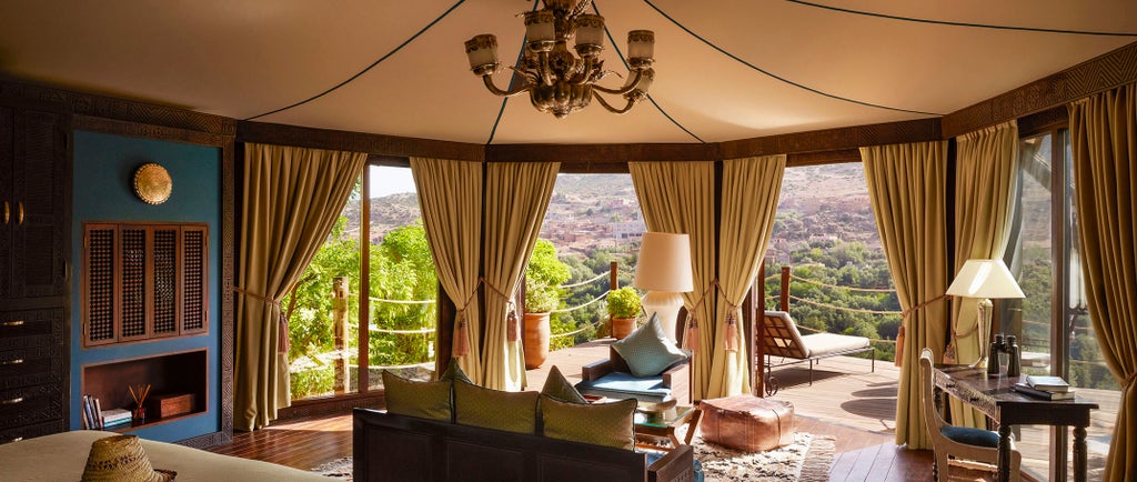 Luxury Moroccan hotel with red clay buildings and swimming pool nestled in Atlas Mountains, surrounded by lush gardens and palm trees