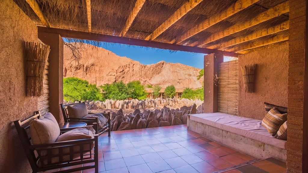 Adobe-style desert lodge with infinity pool framed by red mountains, rustic wooden decks, and native landscaping at dusk