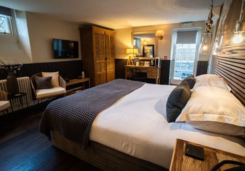 Elegant boutique hotel room with plush white bedding, modern minimalist decor, soft lighting, and panoramic countryside views in rural UK setting