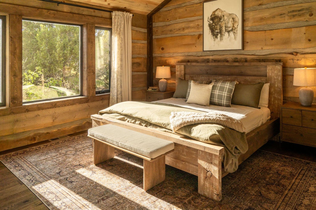 Rustic lodge room with wooden furnishings, plush bedding, and large windows overlooking scenic mountain landscape at scenic Mountain Ranch retreat