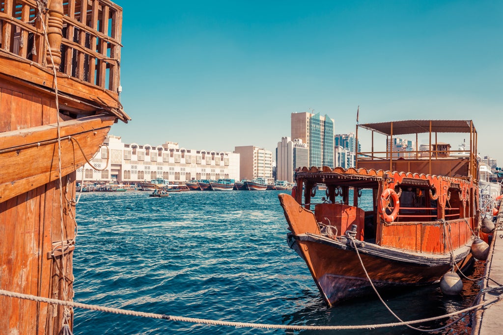 Traditional wooden dhow cruise boat illuminated at night along Dubai Creek, with city skyline and modern buildings in the background