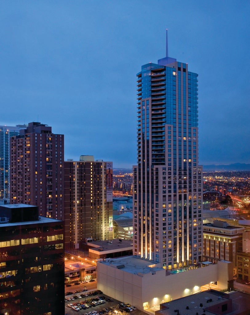 Luxurious Four Seasons Denver high-rise hotel with modern glass facade, illuminated at night against city skyline, reflecting urban lights