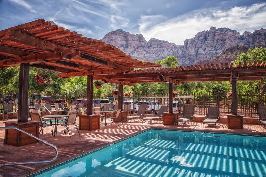 Luxurious mountain lodge exterior with stone facade, floor-to-ceiling windows, and wooden beams nestled against dramatic red cliffs