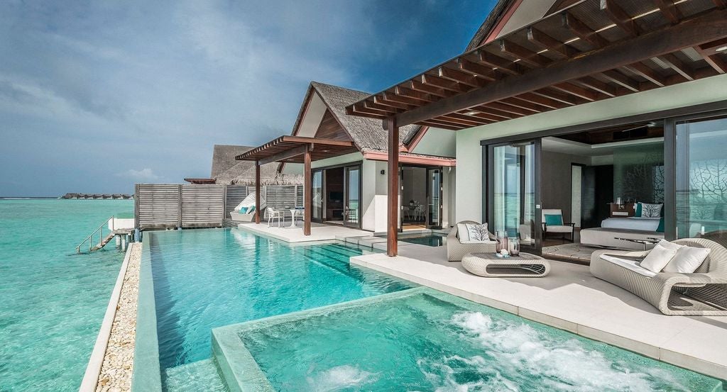 Luxurious water villa perched on stilts over crystal-clear turquoise lagoon in Maldives, with private infinity pool and wooden deck