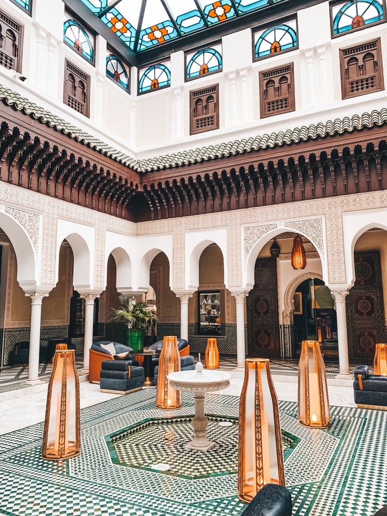 Ornate Moroccan archway framing lush courtyard garden at La Mamounia hotel, with traditional tile work and lantern lighting at dusk