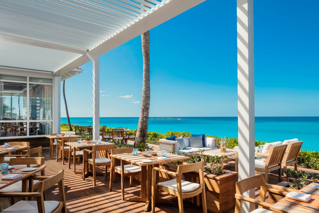 Luxurious beachfront hotel with white exterior and palm-lined walkway, overlooking turquoise Caribbean waters and pristine sandy beach